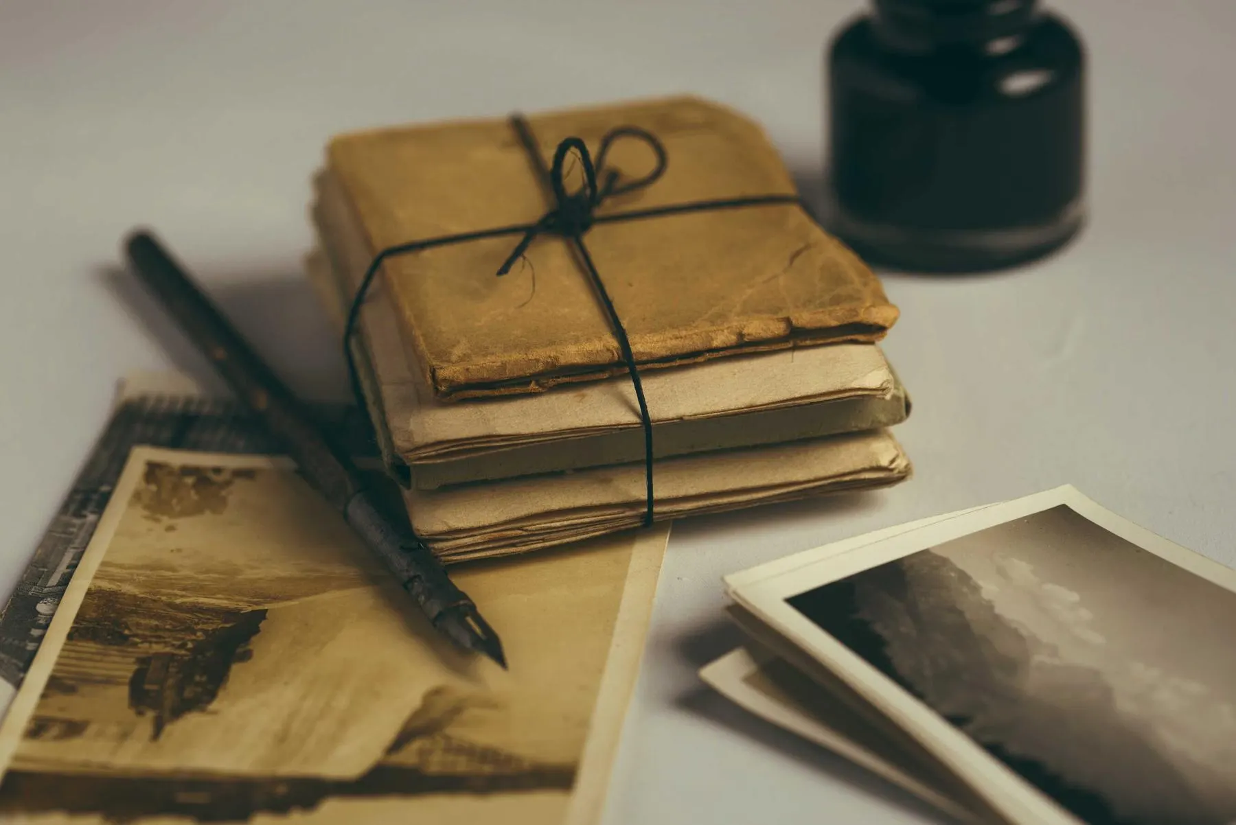 A bundle of old letters tied with string, a pen, an ink bottle and black-and-white photographs on a table.