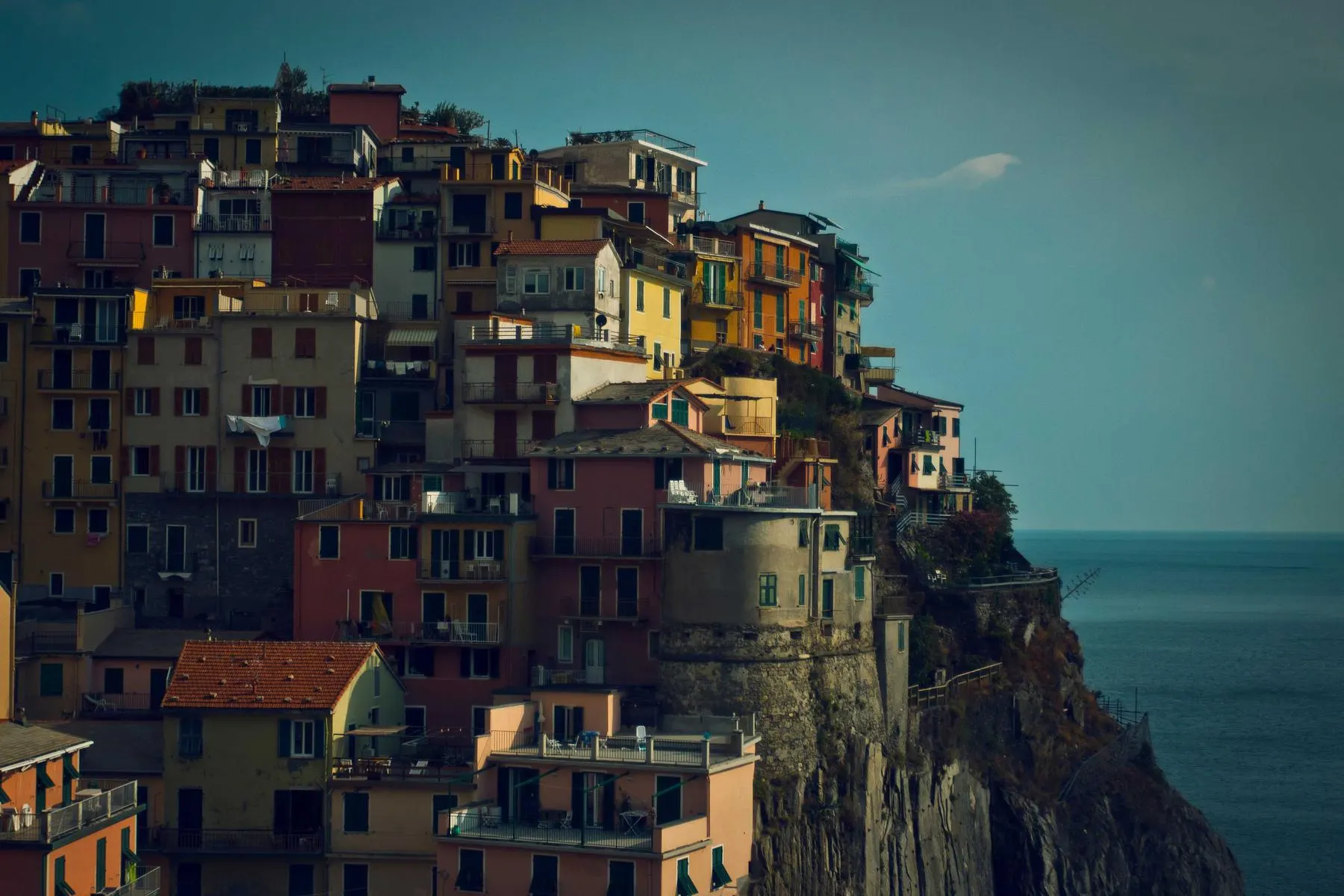 Tall, colourful houses stacked on a cliff above the sea in late evening light.