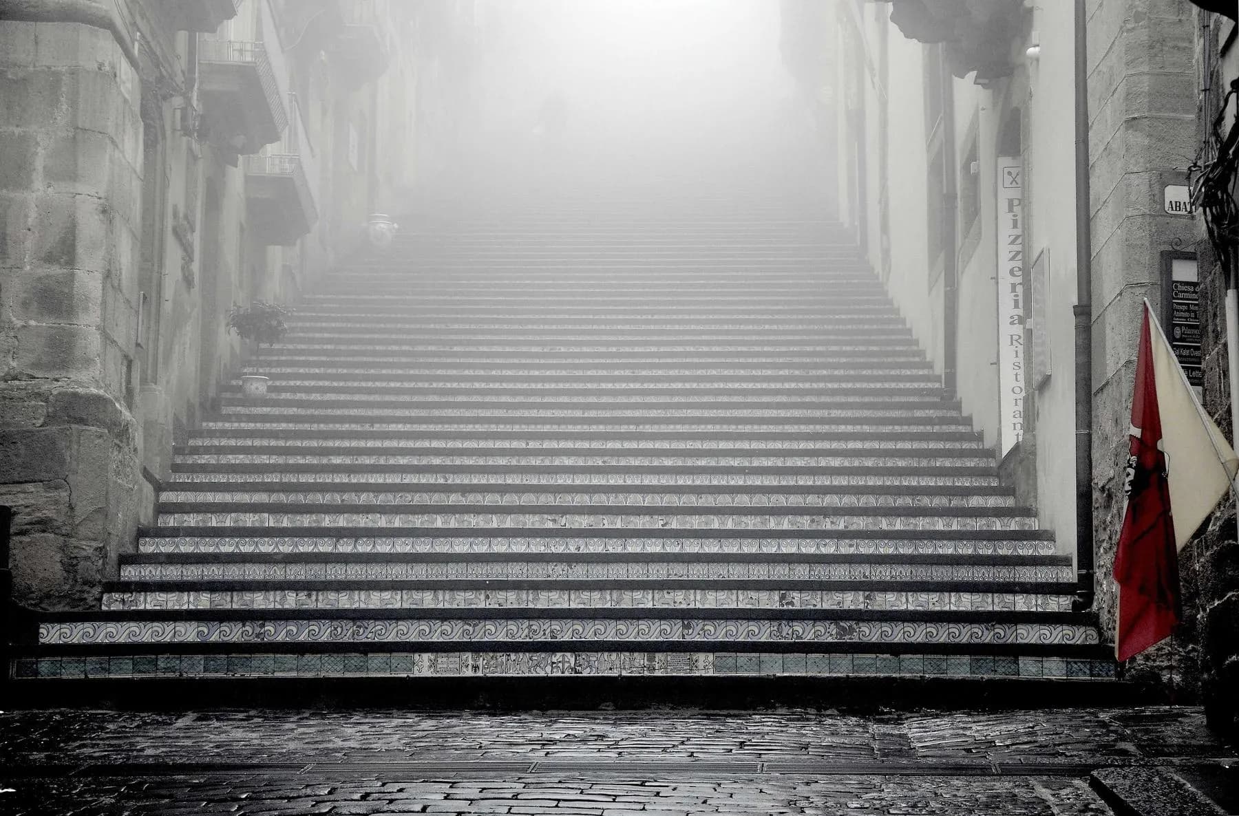 A long flight of stone steps climbing between old walls and disappearing into fog.