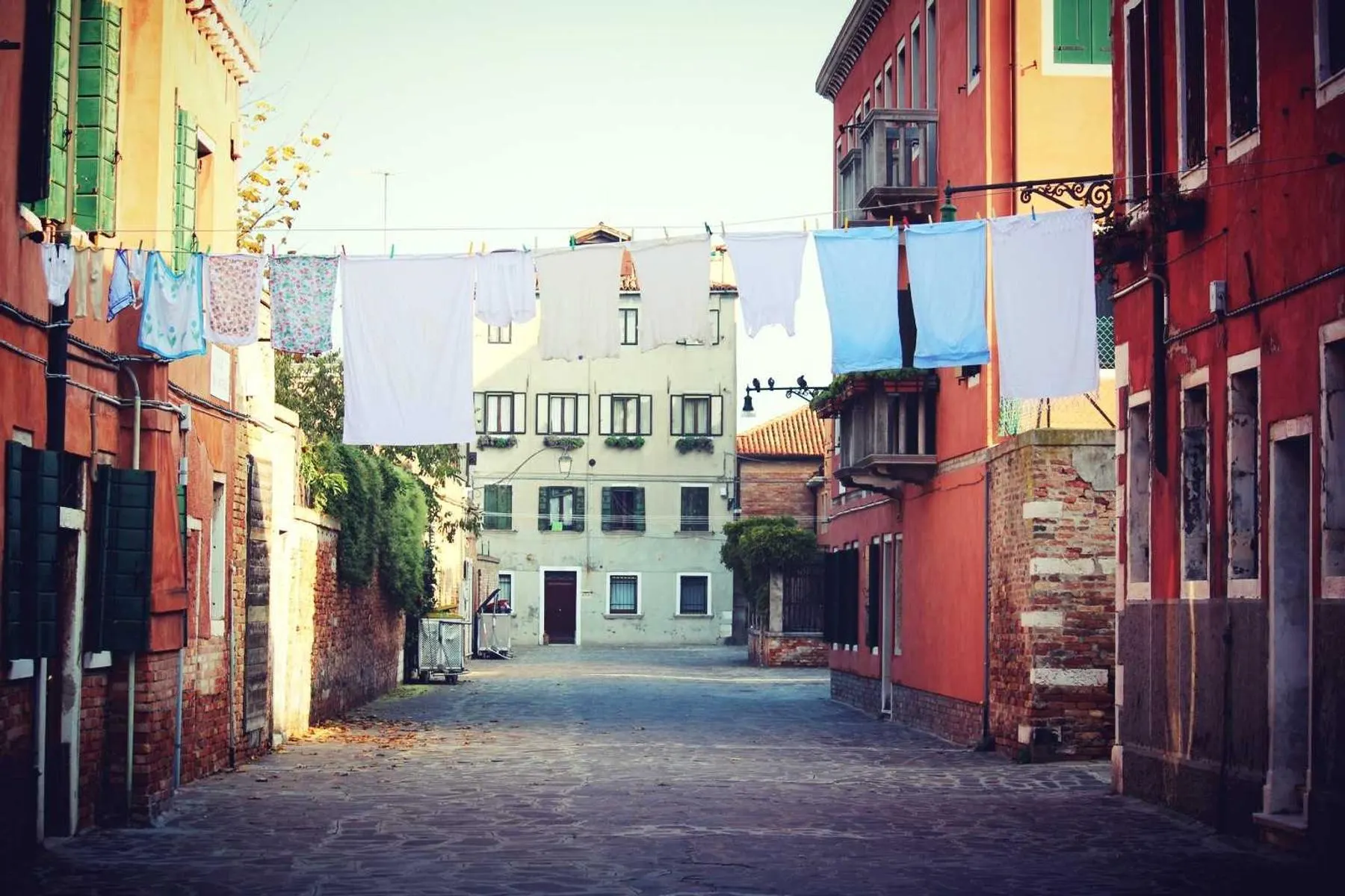 A narrow street between brightly painted houses with laundry hanging on lines strung across from window to window.